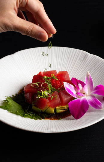 Chef sprinkles garnish on tuna sashimi on white plate with orchid Sakana