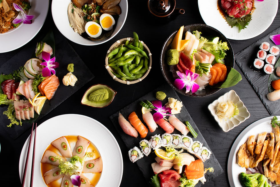 Assortment of sushi, sashimi, ramen, edamame, and flowers on a black table.