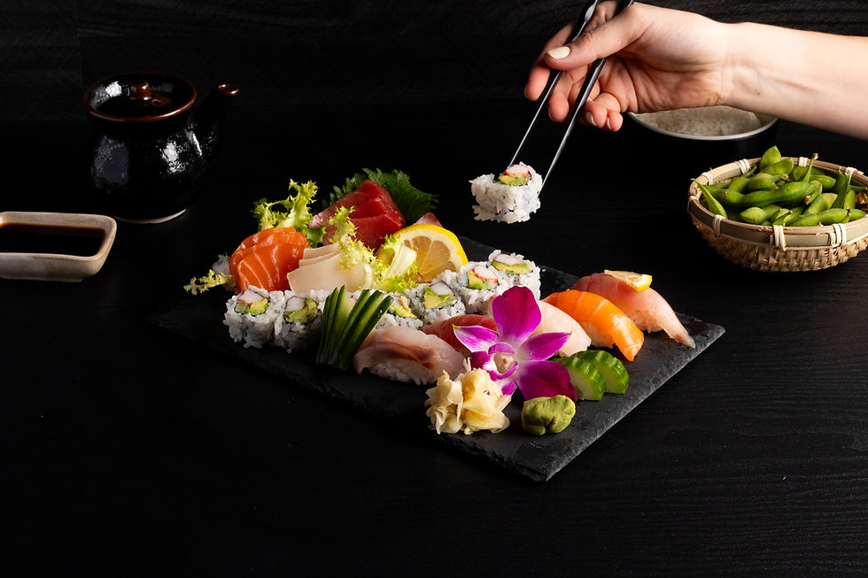 Hand using chopsticks to pick sushi roll from assorted Japanese food Sakana